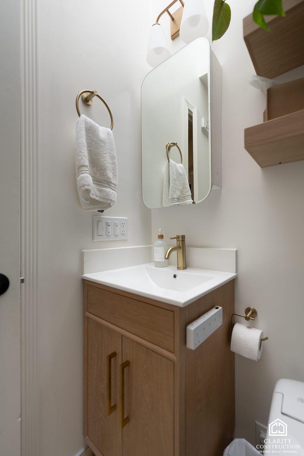 Oak vanity with a white top under an arched mirror and oak shelves