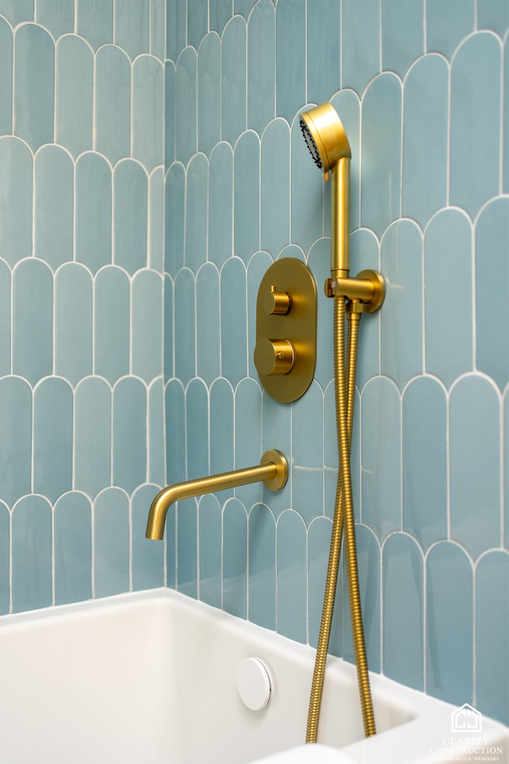 Brass hand shower and tub filler against blue picket tile