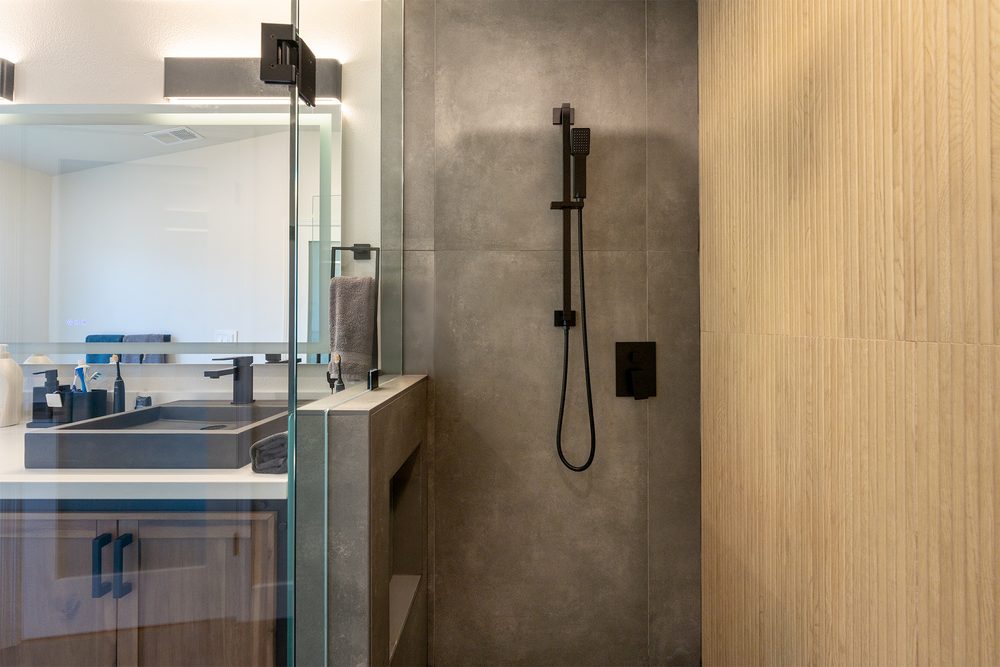 Charcoal tile shower wall with a black hand shower and wood-look accent