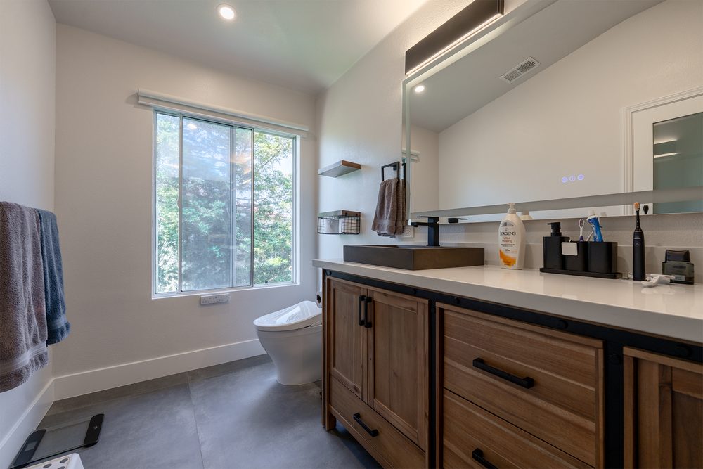 Walnut vanity with a vessel sink and a backlit mirror under a window