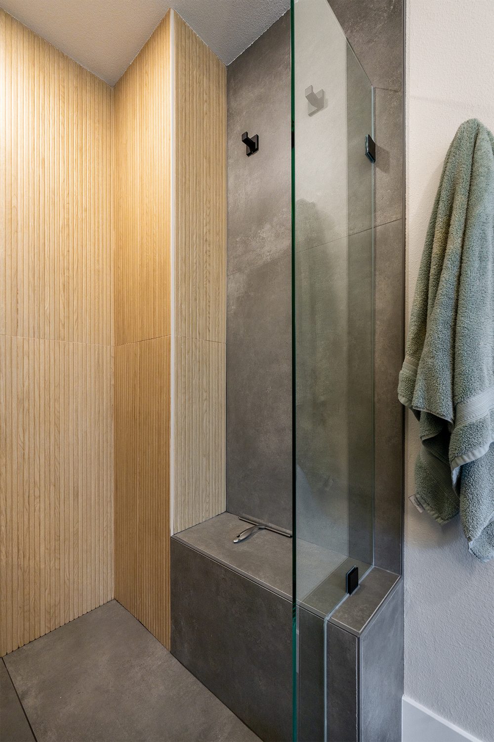 Shower bench in charcoal tile beside a wood-look wall