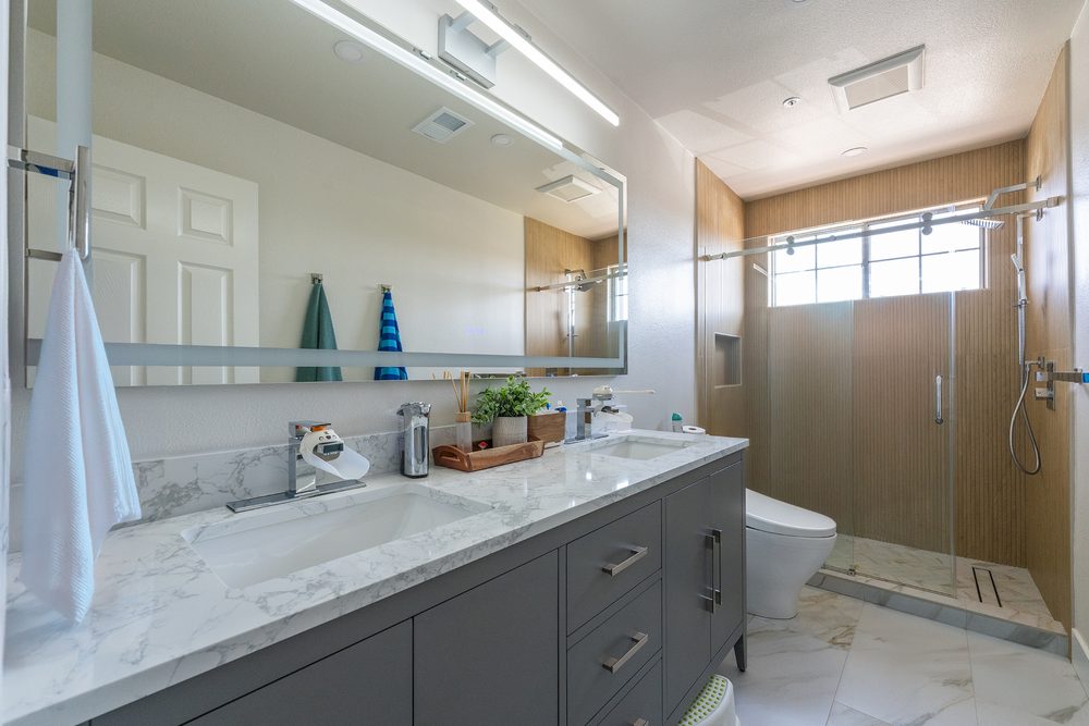 Gray shaker vanity with a marble counter and a wood-look tile shower