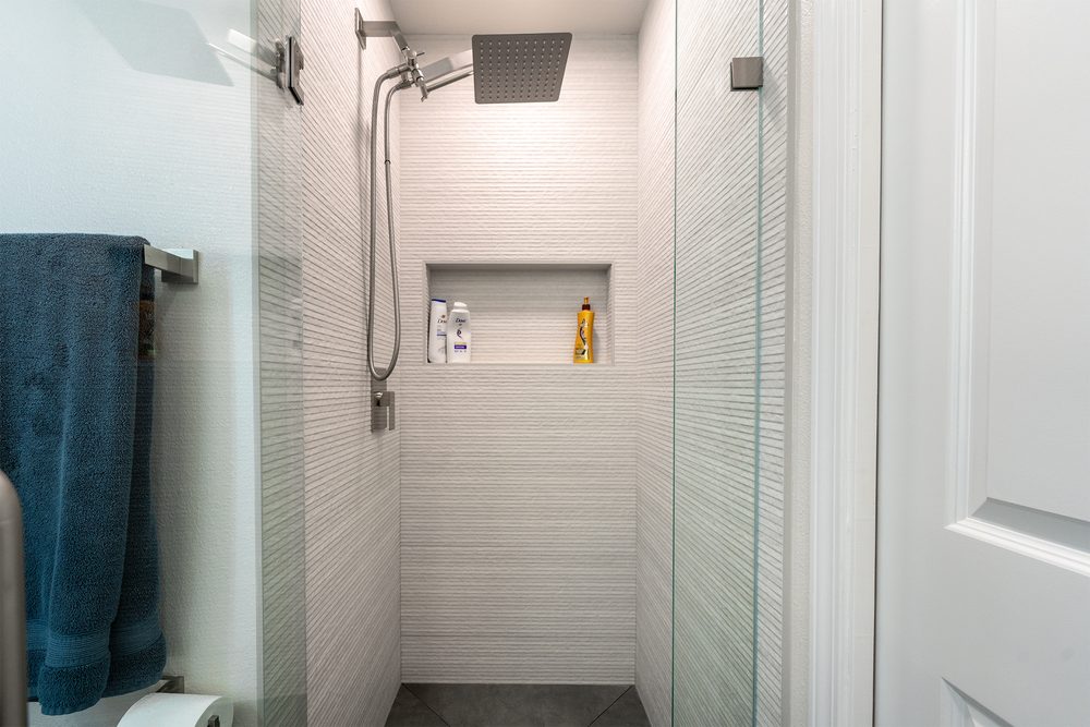 White textured tile shower with a rain head and a recessed niche
