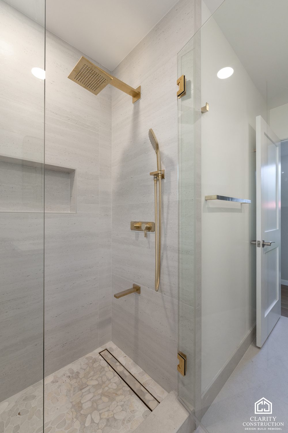 Brass rain head and hand shower on the stone-look tile shower wall