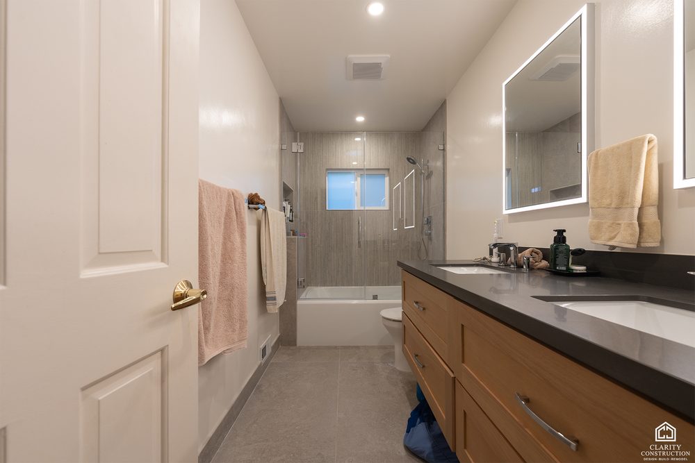 Oak double vanity with two sinks and backlit mirrors beside the tub
