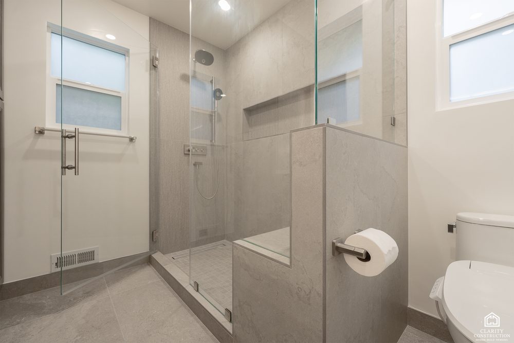 Walk-in shower with a tiled bench and a half wall beside the toilet
