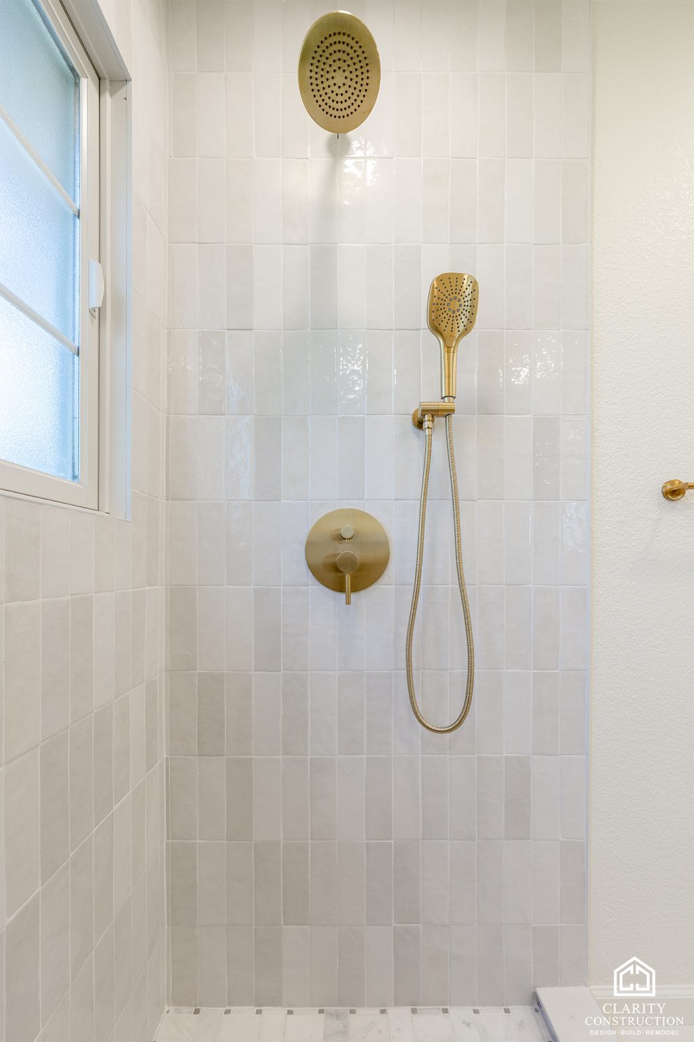 Brass rain head and hand shower on the glossy tile wall