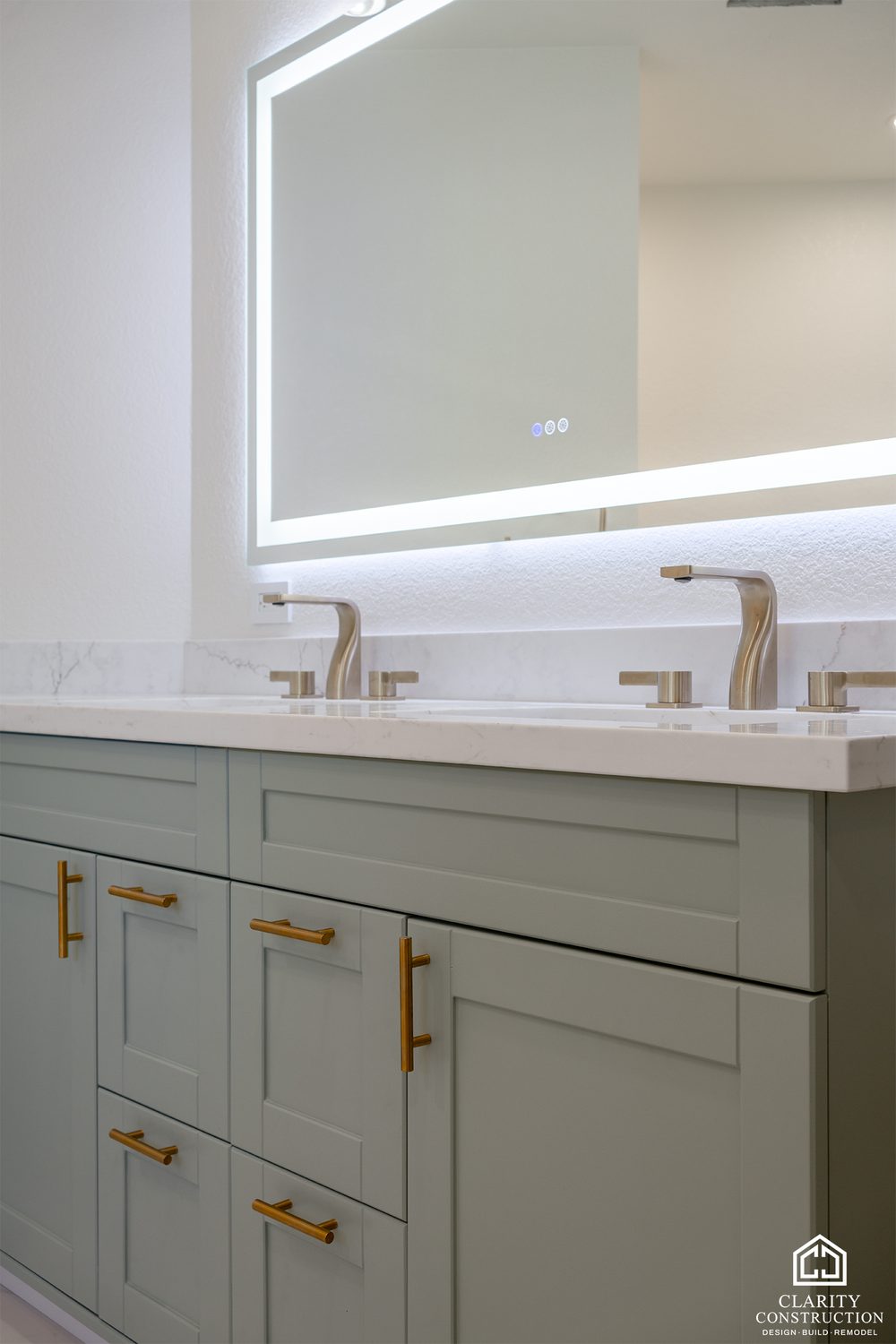 Backlit mirror over the sage green vanity with brass faucets