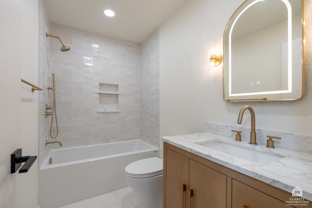 Guest bathroom with an arched backlit mirror, an oak vanity and a tiled tub