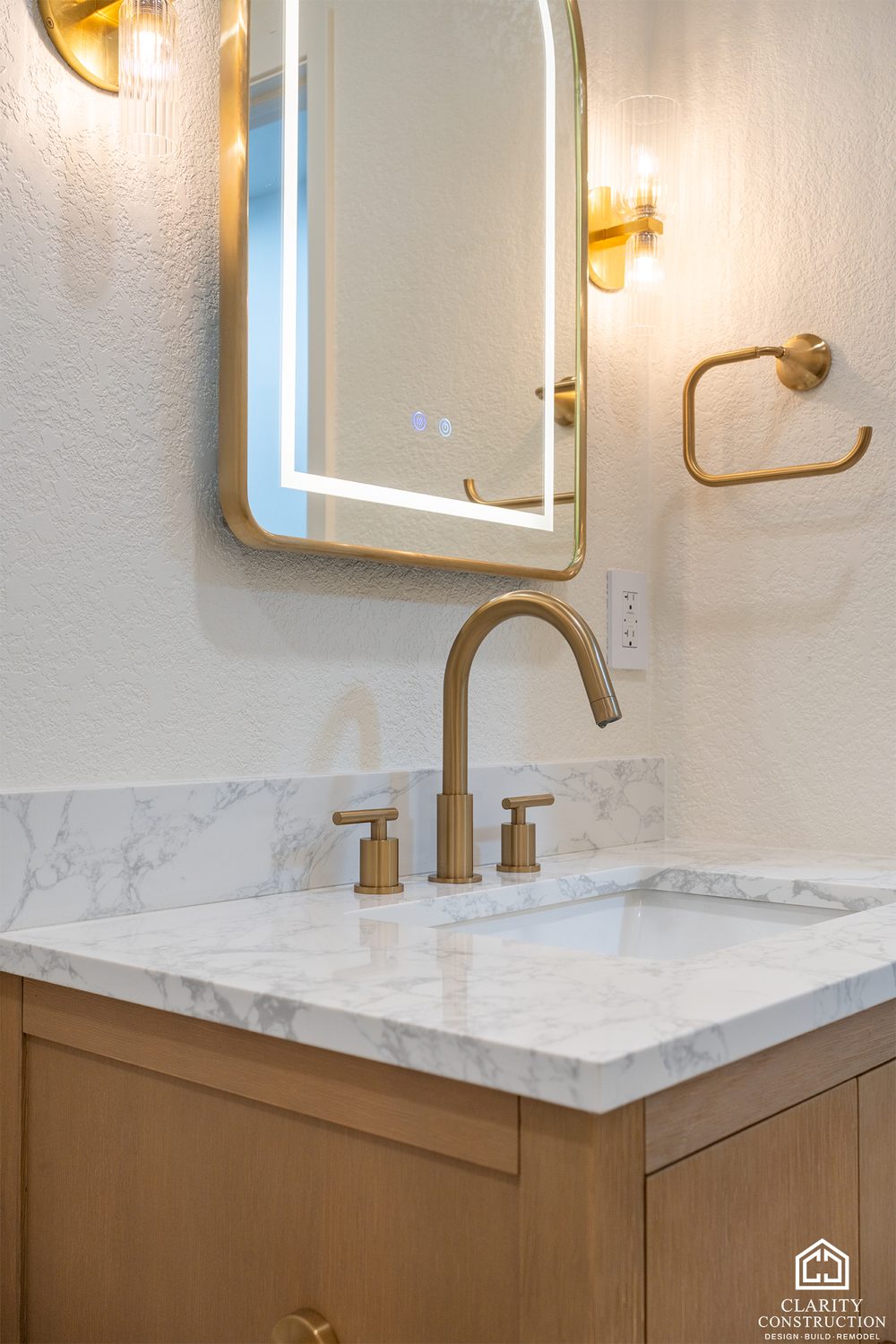 Arched backlit mirror and brass faucet over the oak vanity
