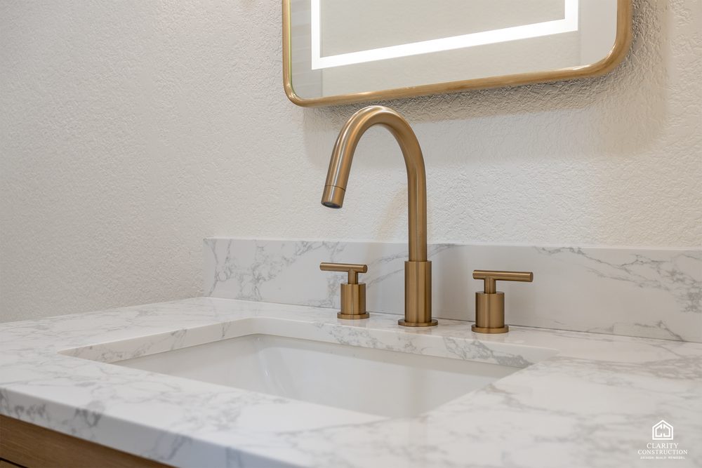 Brass widespread faucet on a marble-look counter under the arched mirror