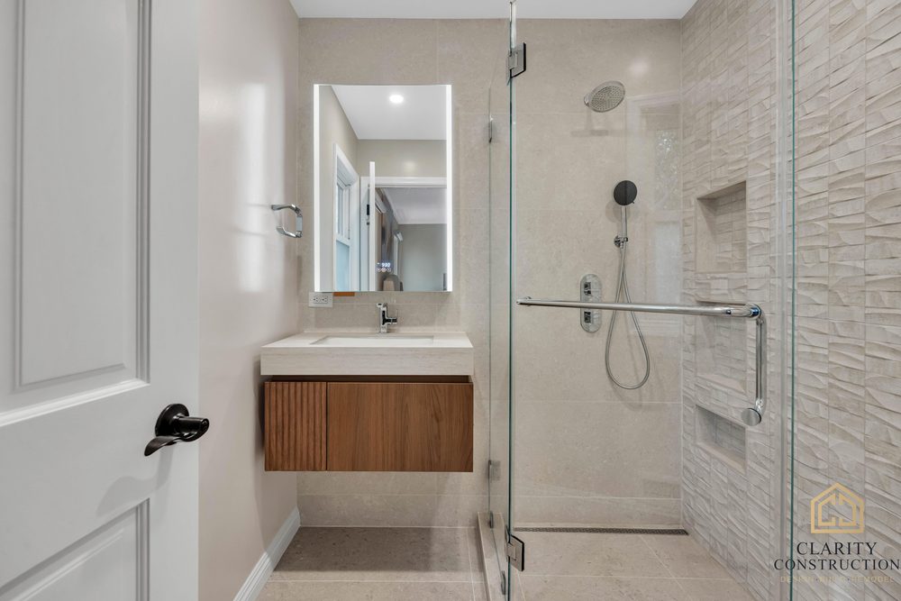 Bathroom with a floating walnut vanity, backlit mirror and a curbless walk-in shower behind frameless glass
