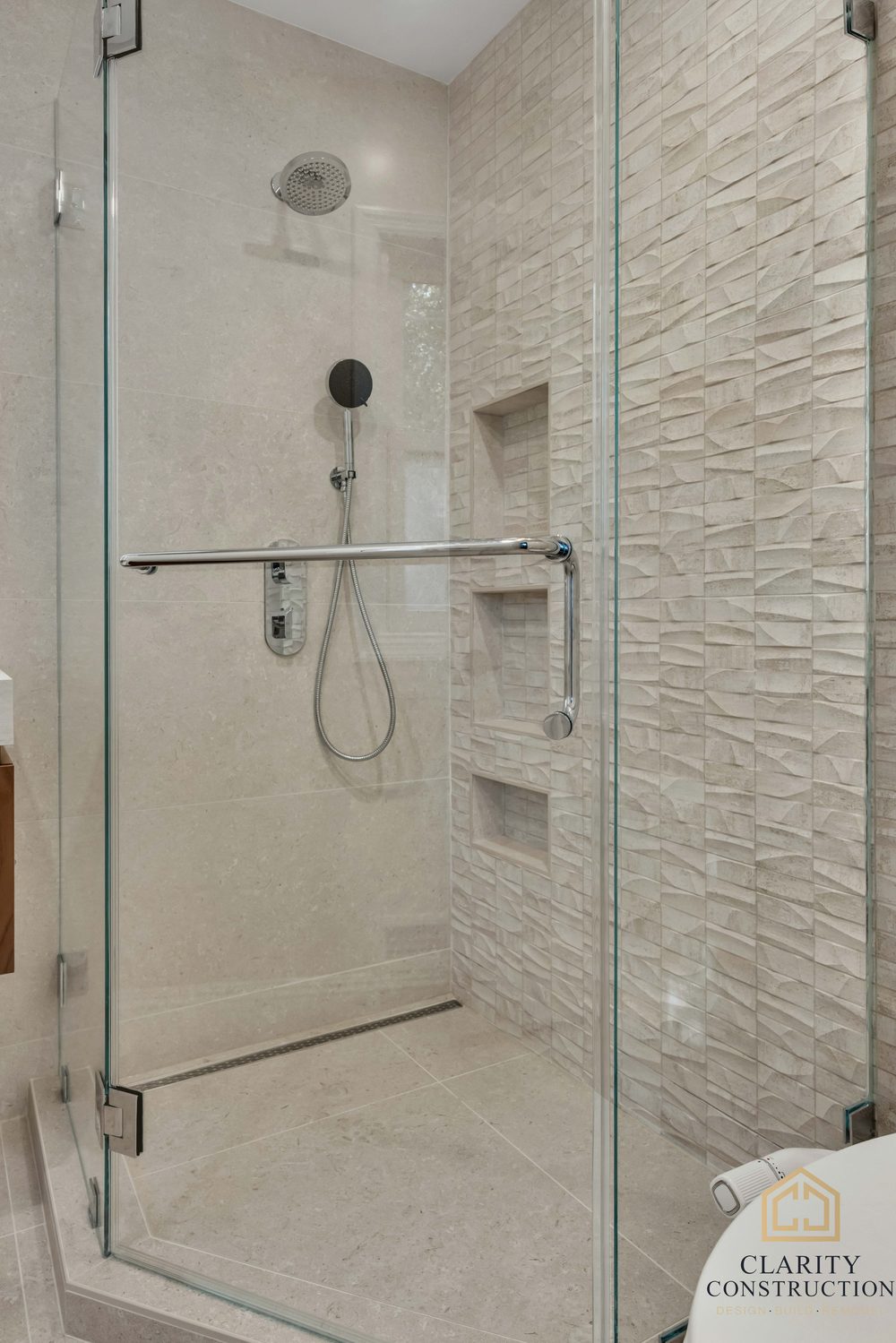 Inside the walk-in shower: rain head, hand shower and a textured tile wall with niches