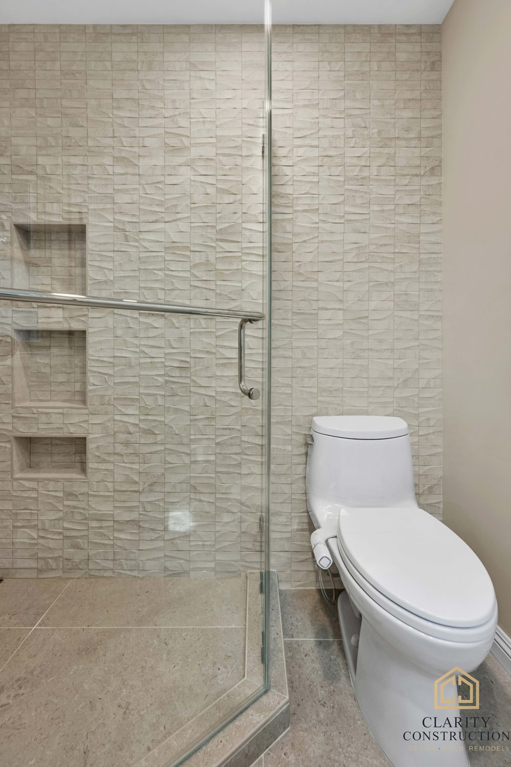 Textured stone-look tile wall with three niches running past the glass to the toilet