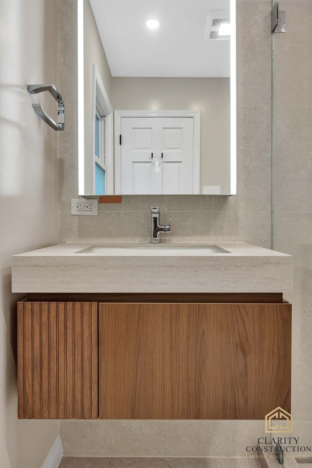 Floating walnut vanity with a fluted door, quartz top and chrome faucet under a backlit mirror