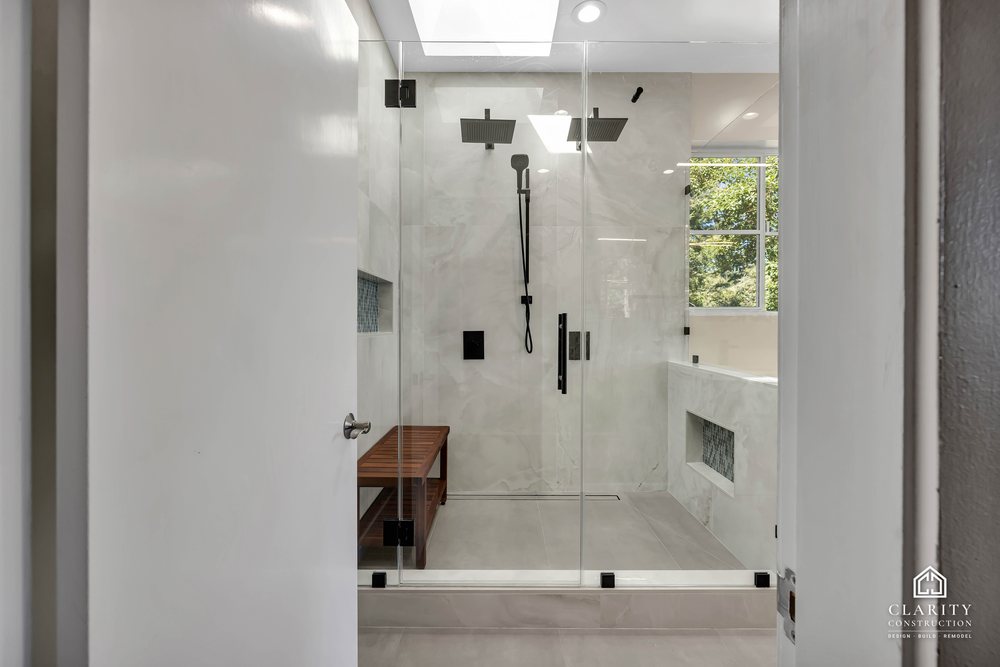 Walk-in shower with a teak bench, black fixtures and a window to the trees