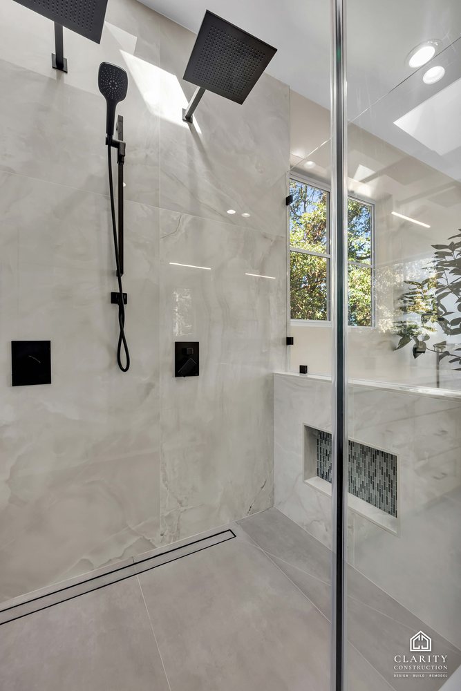 Marble-look shower wall with a black rain head under the skylight