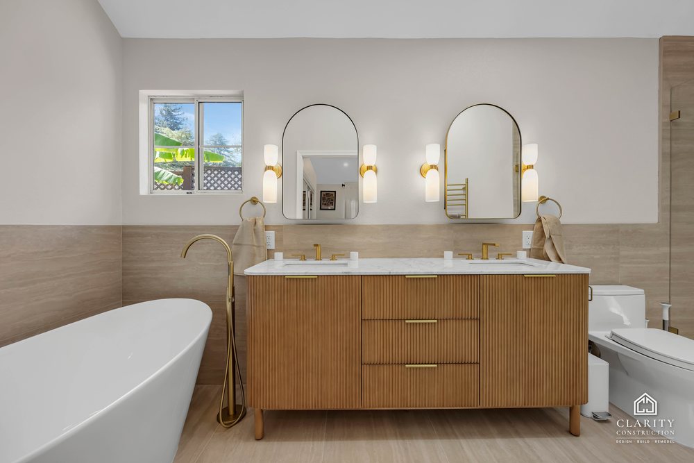 Primary bath: freestanding tub under the window beside the fluted oak double vanity with arched mirrors