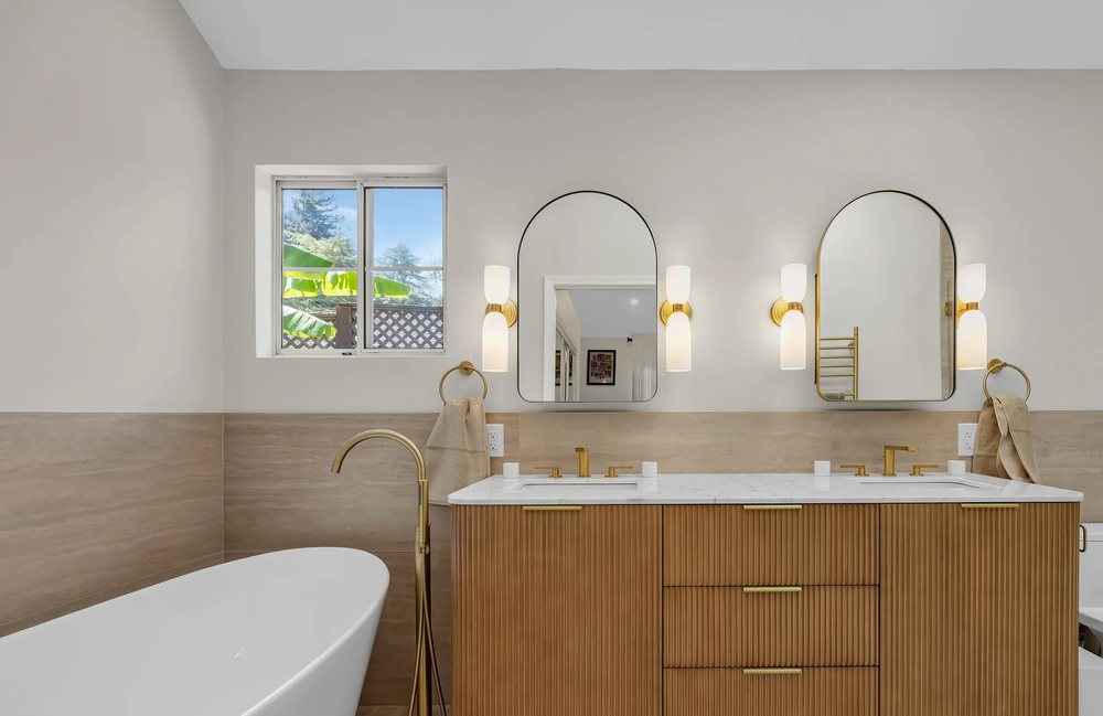 Remodeled Los Gatos primary bathroom with a freestanding tub, fluted white oak double vanity and arched brass mirrors