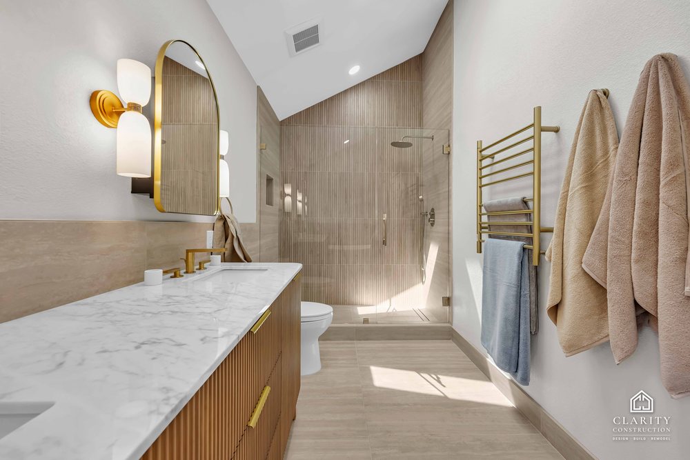 Primary bath: walk-in shower with a brass towel rail, vanity in the foreground
