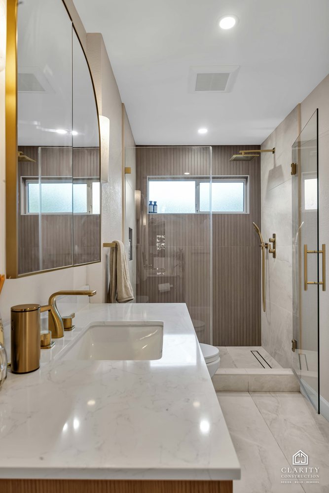 Hall bath: walk-in shower behind frameless glass with brass fixtures