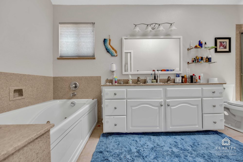 Before: the primary bath with a white vanity, built-in tub and corner shower stall