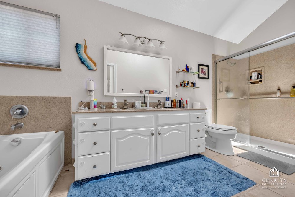 Before: the primary bath with a white vanity, built-in tub and corner shower stall