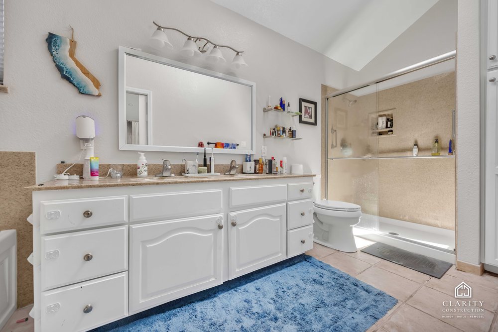 Before: the primary bath with a white vanity, built-in tub and corner shower stall