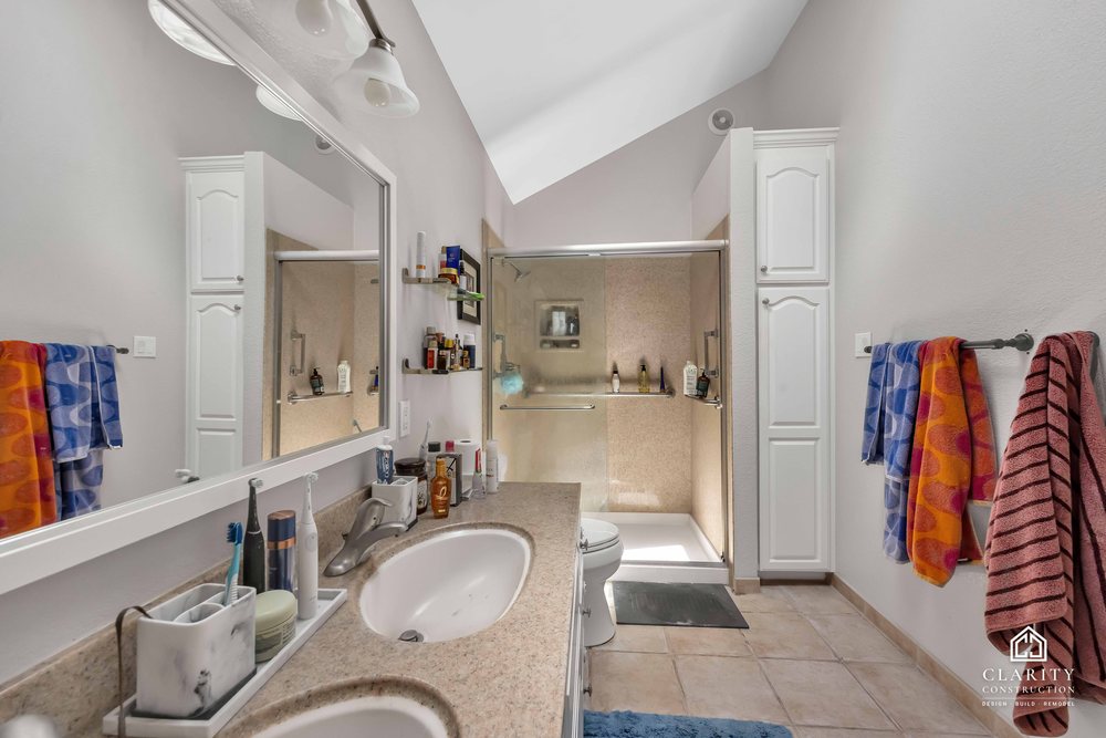 Before: the primary bath with a white vanity, built-in tub and corner shower stall